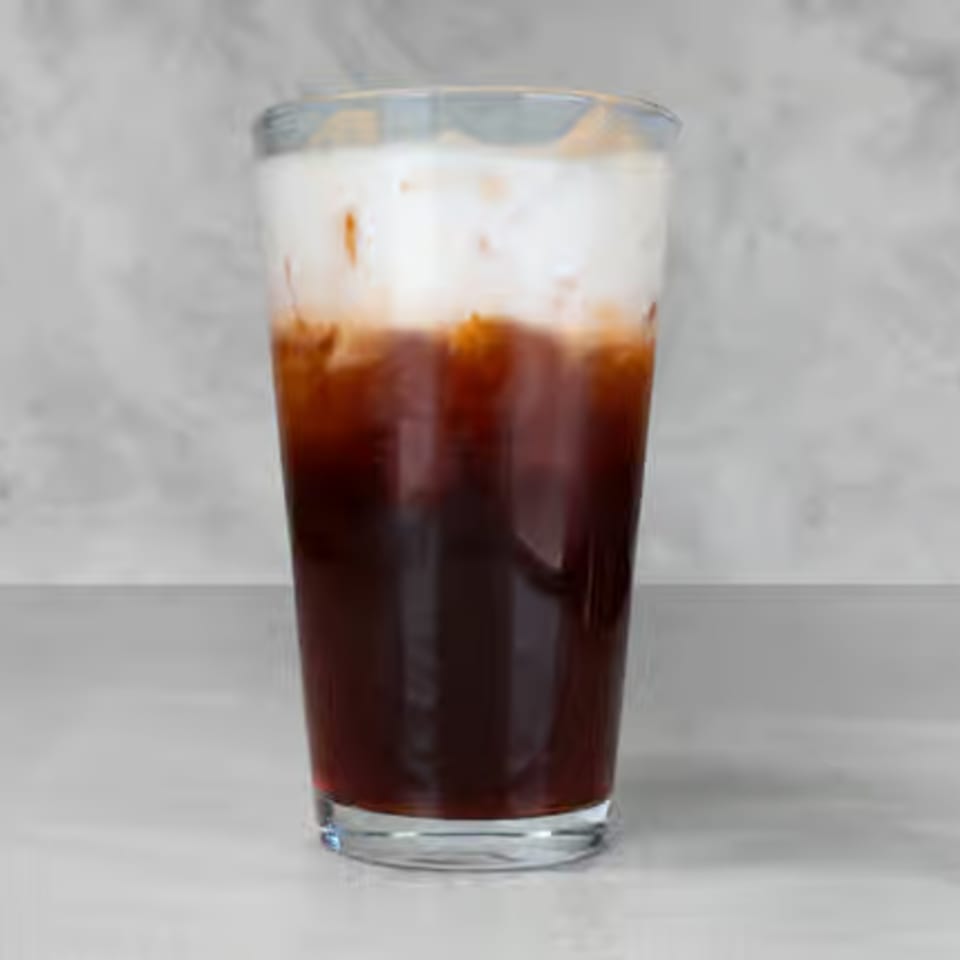 A tall glass of iced Thai tea with a dark amber base and a creamy white top layer.