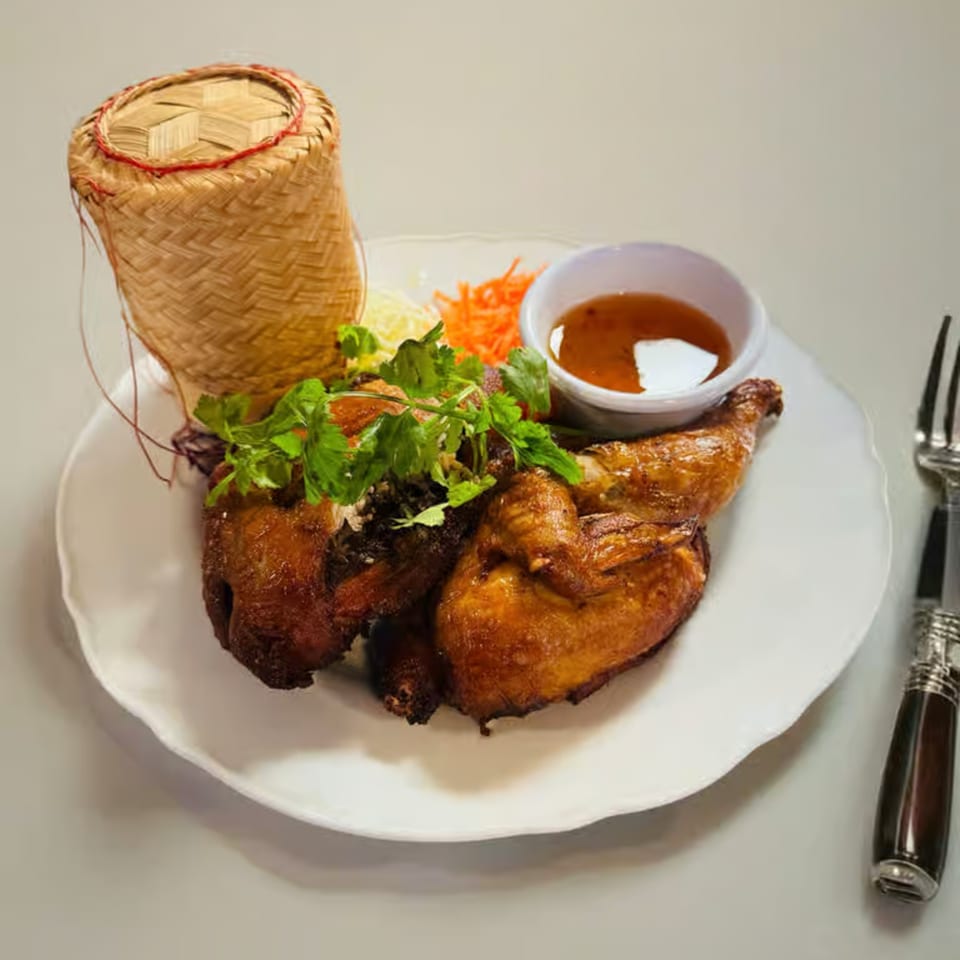 Golden brown roasted chicken with cilantro, shredded vegetables, dipping sauce, and a bamboo rice container.