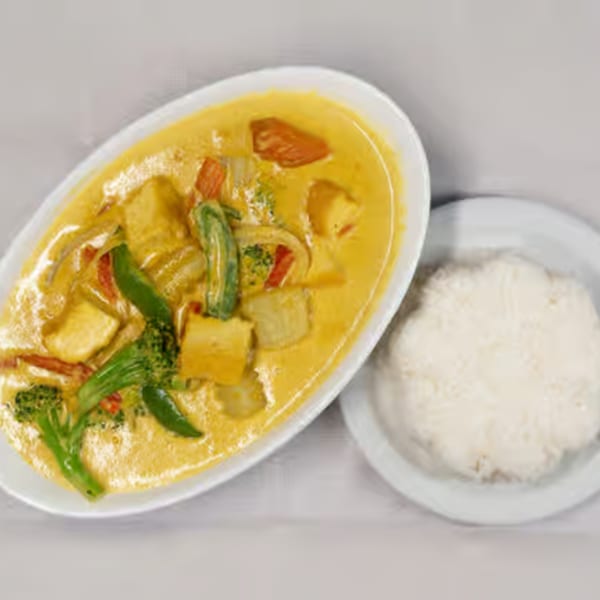Yellow curry with vegetables and tofu in a white bowl, served with a side of white rice.