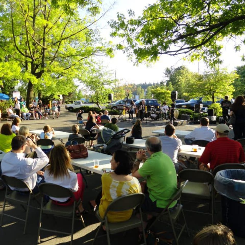 People seated at tables outdoors, watching a band perform under green trees at Rice Thai Cookery.