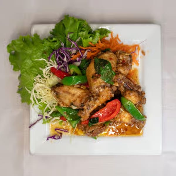 Thai chicken wings with red and green peppers, basil, and shredded vegetables on a white plate.