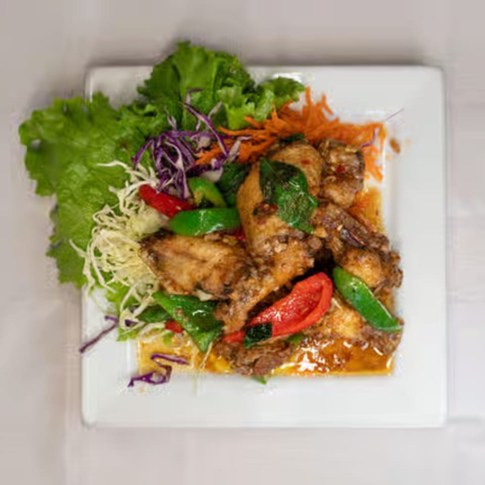 Thai chicken wings with red and green peppers, basil, and shredded vegetables on a white plate.