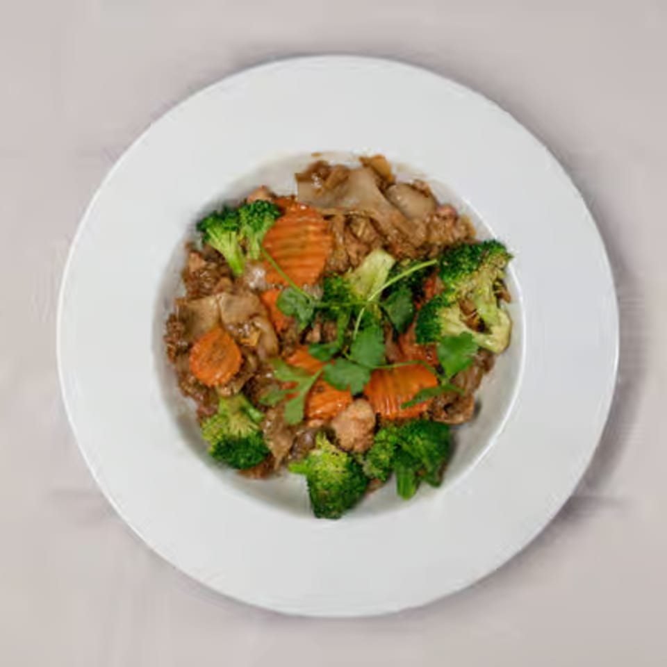 Thai stir-fry with broccoli, carrots, and meat, garnished with cilantro on a white plate.