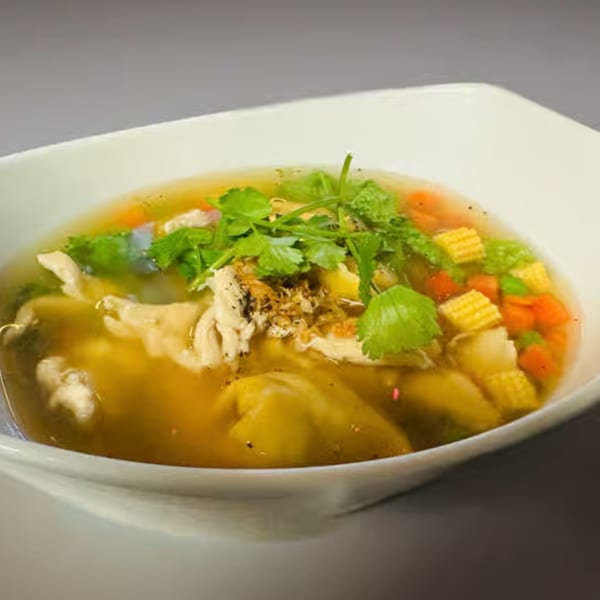 A bowl of clear Thai soup with chicken, baby corn, carrots, and fresh cilantro.